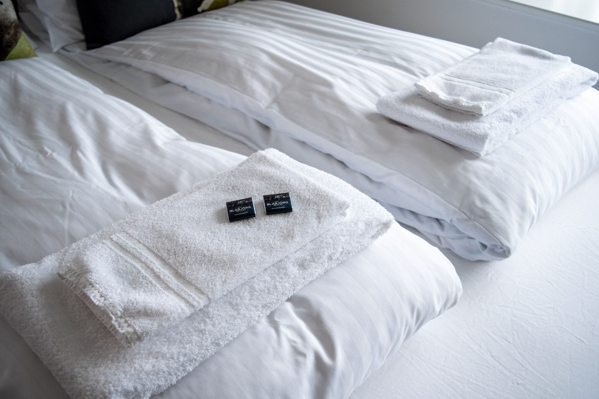 Un lit bien fait, avec du linge de lit blanc et deux serviettes noires et dorées posées sur le côté.