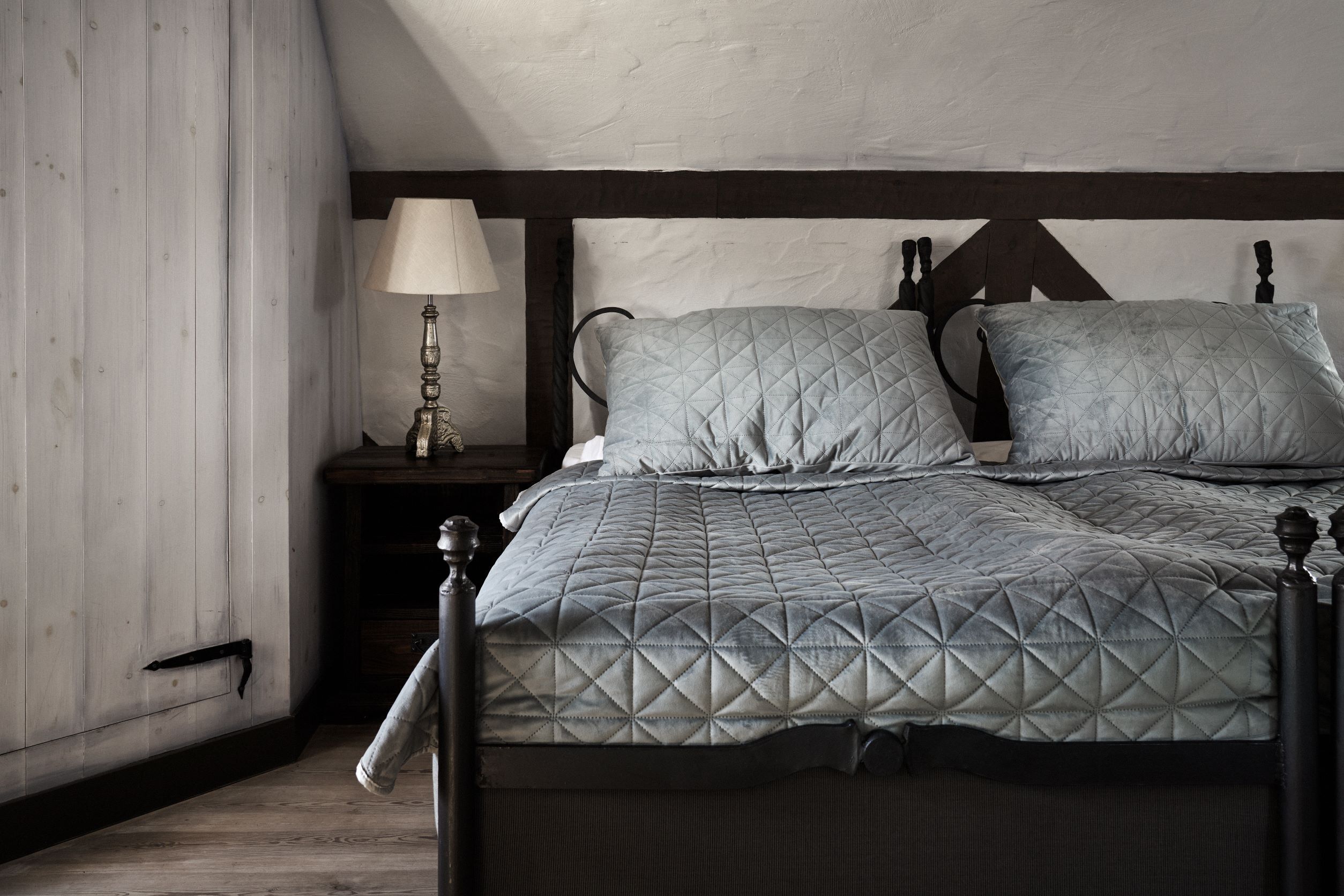 Un dormitorio con cama, mesita de noche, lámpara y cabecera de madera.