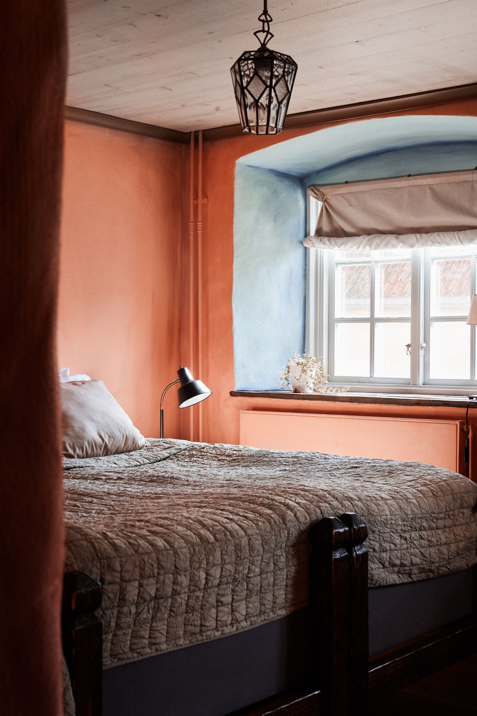 Un dormitorio con una cama, una mesita de noche, una lámpara, una ventana con vistas y una lámpara colgante.