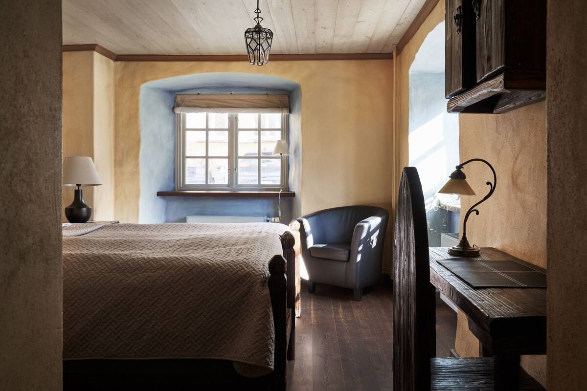 A bedroom with a bed, a chair, a desk, and a window.