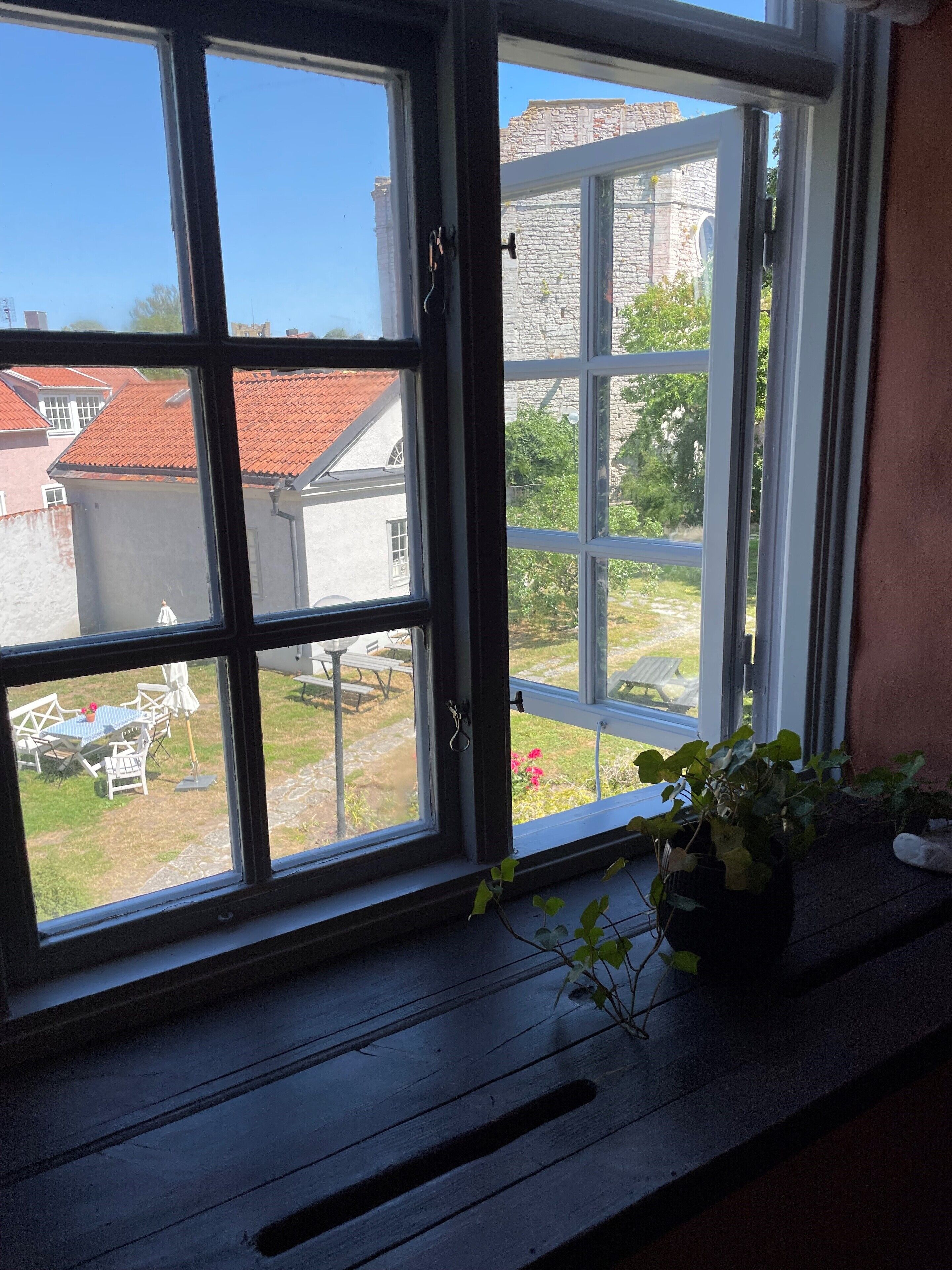 A window with a view of a garden, a stone building, and a red-roofed house.