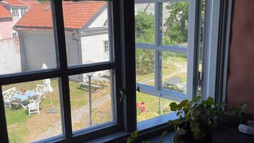A window with a view of a garden, a stone building, and a red-roofed house.