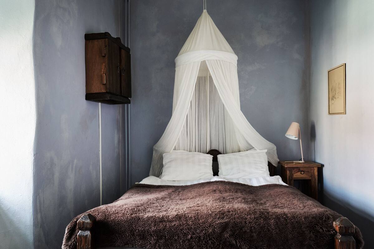 A bedroom with a canopy bed, a wooden cabinet, and a bedside table with a lamp.