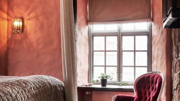 A room with a four-poster bed, a red armchair, a window with a view, and a wall-mounted light fixture.