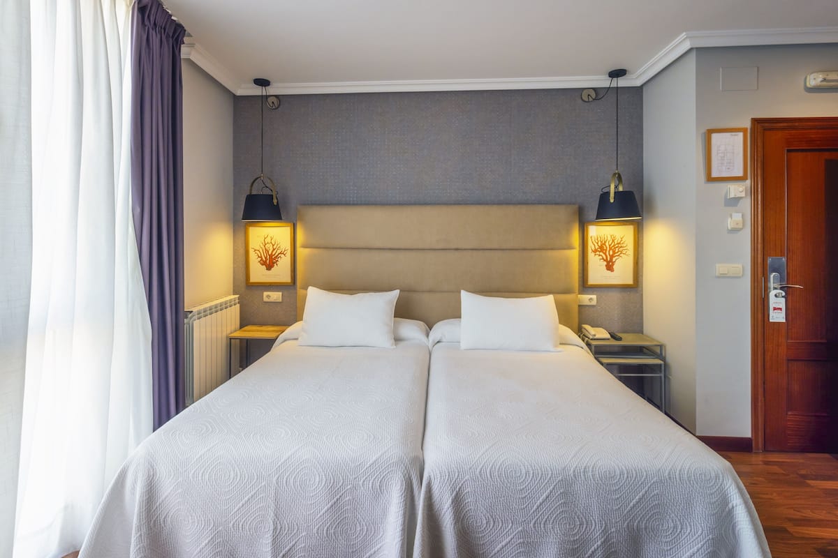 Una cama doble con dos mesitas de noche, cada una con una lámpara, en una habitación de hotel con puerta de madera y radiador.