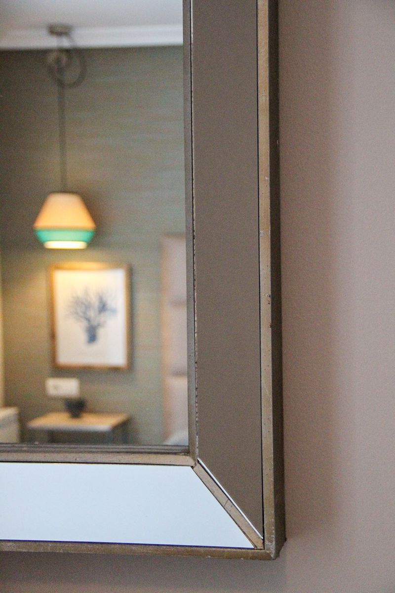 A mirror reflecting a bathroom interior with a framed picture on the wall.