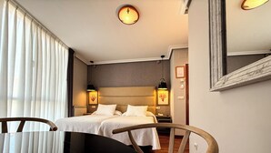 Una habitación de hotel con dos camas, una silla de madera, una mesita pequeña y un espejo grande.