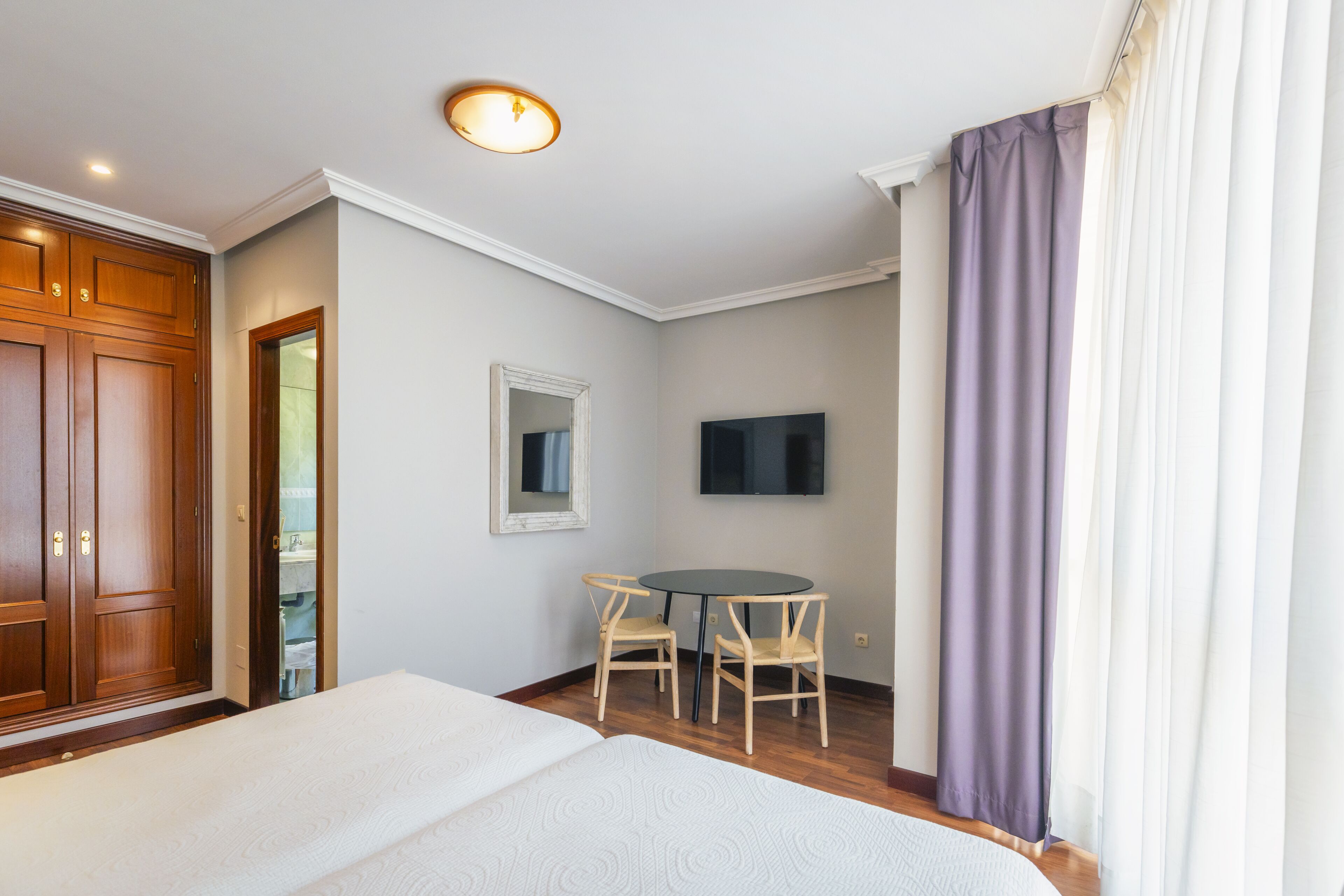 A hotel room with a bed, a desk with two chairs, a TV, and a wooden wardrobe.
