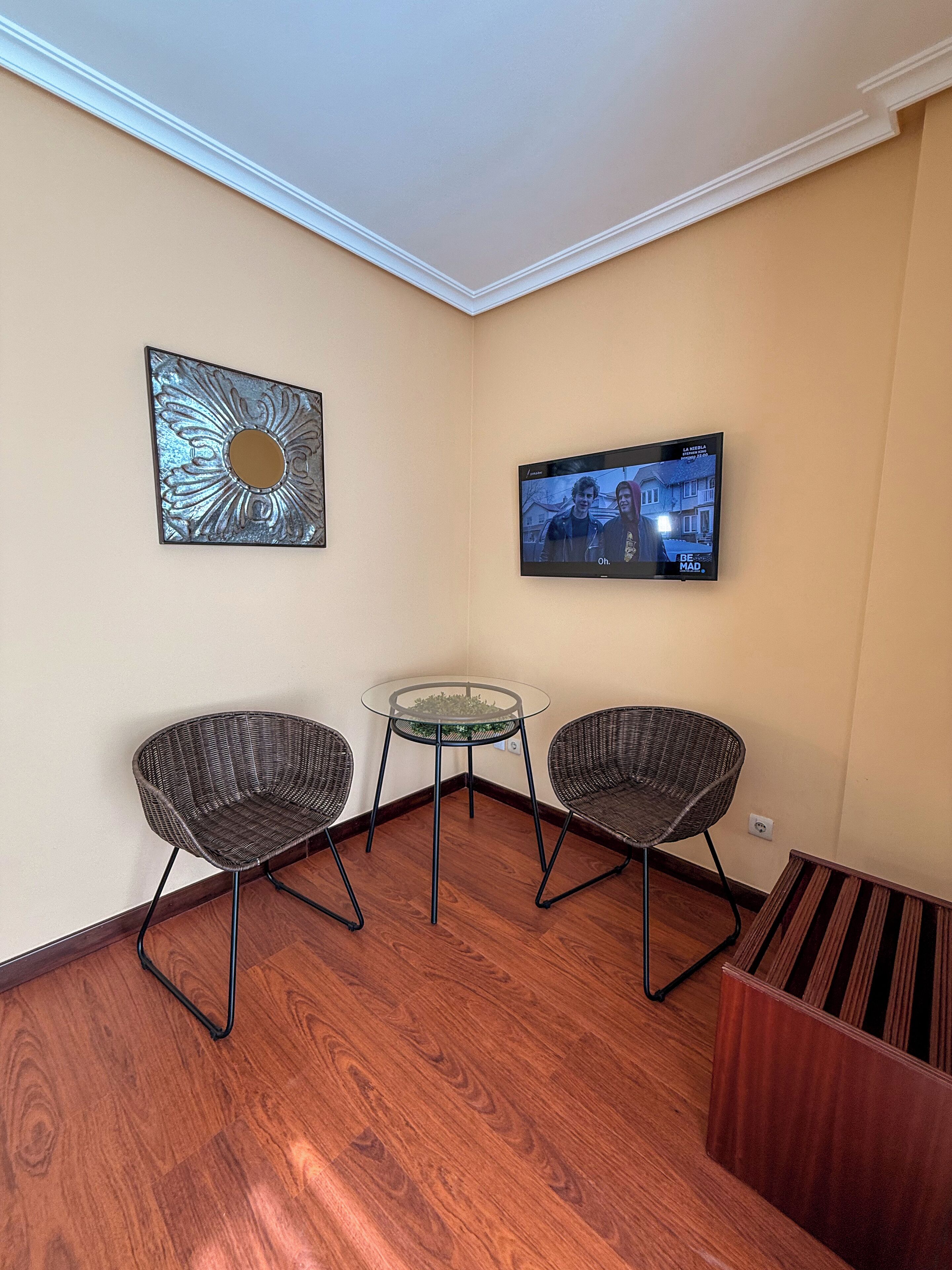 Ein Wohnzimmer mit zwei Korbstühlen, einem Glastisch, einem flachbildfernseher an der Wand und einem dekorativen Metallkunstwerk.