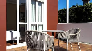 An outdoor patio with two wicker chairs and a table, a building with large windows, and a clear blue sky.