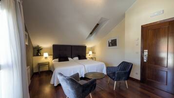 A hotel room with two beds, a small table, two chairs, a wooden door, and a ceiling light.