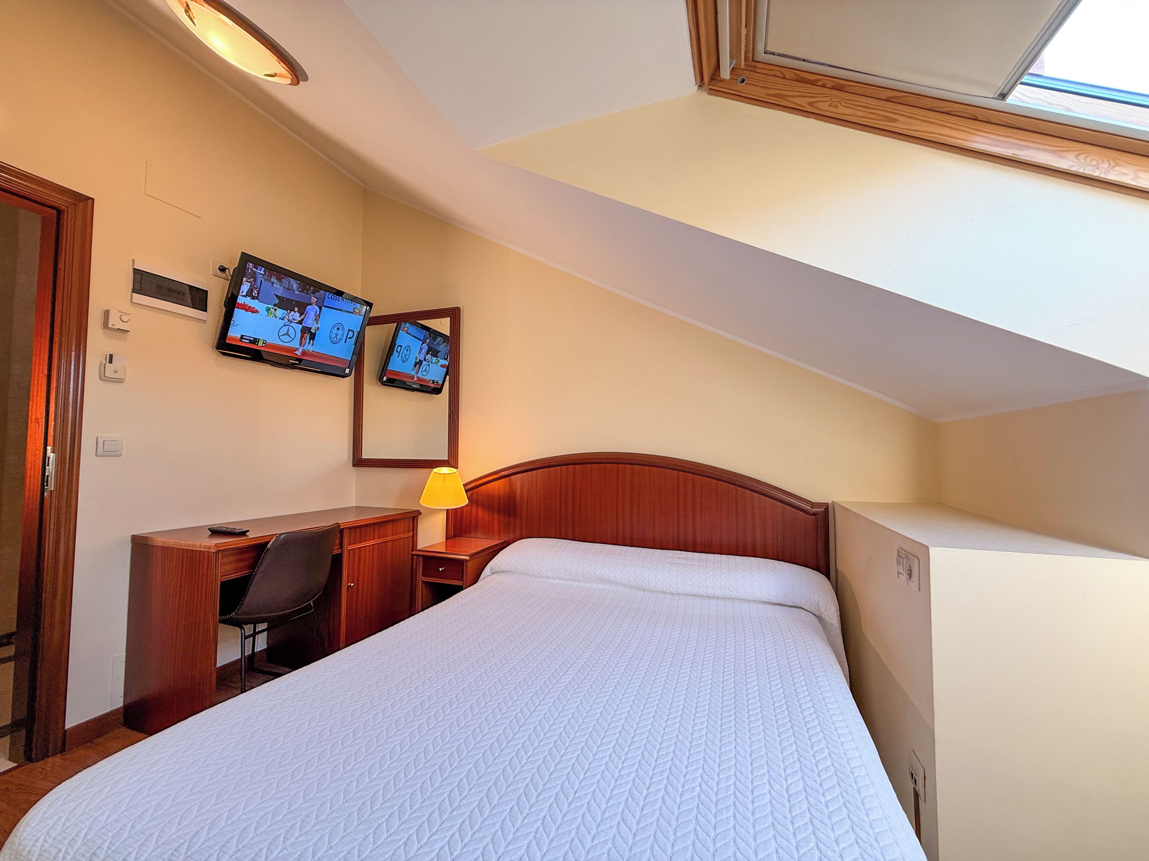 Habitación de hotel con cama, escritorio y dos monitores en la pared.