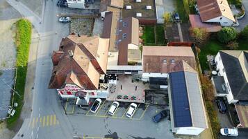 An aerial view of a parking lot with several cars, a building with a sloped roof, and a small green area.
