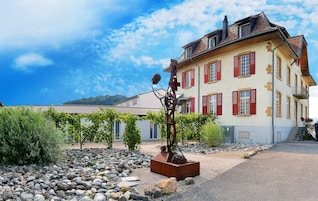A building with red shutters, a stone facade, and a garden with a metal sculpture.