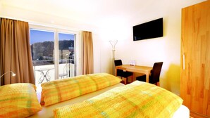 A hotel room with two beds, a dining table, and a TV on the wall.