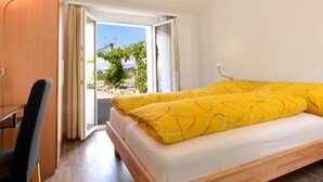 A bedroom with a bed, a desk, and a view through a glass door.