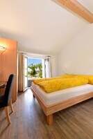 Quarto com cama, escrivaninha e vista através de uma porta de vidro.