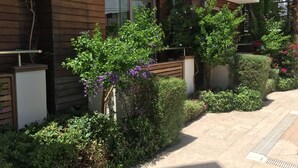A modern building with wooden paneling, a well-maintained garden with various shrubs and flowers, and a paved walkway. - Butikhan Otel (Bodrum)