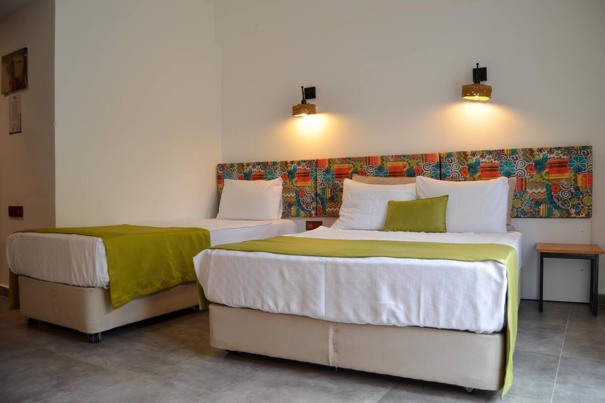Habitación de hotel con dos camas, cada una con una manta verde, ropa de cama blanca y un cabecero colorido.