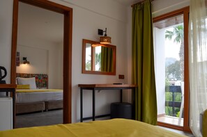 A hotel room with a bed, a table, a mirror, and a view of greenery outside. - Butikhan Otel (Bodrum)