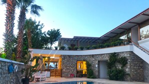 A modern outdoor pool area with a stone wall, a covered seating area, and a staircase leading to an upper level. - Butikhan Otel (Bodrum)