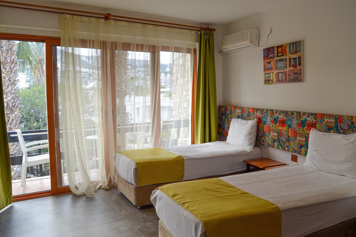 Habitación de hotel con dos camas, un balcón con una silla y un colorido adorno en la pared.