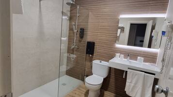 Un baño moderno con ducha de vidrio, inodoro blanco y lavamanos con espejo arriba.
