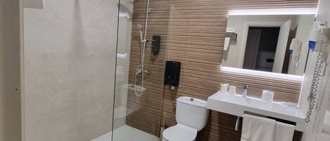 Un baño moderno con ducha de vidrio, inodoro blanco y lavamanos con espejo arriba.