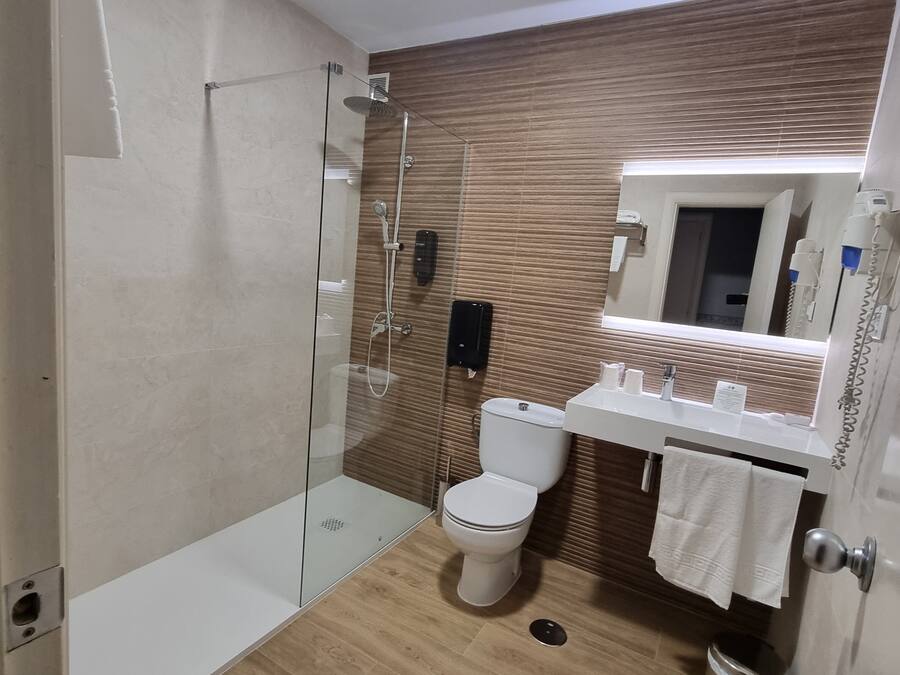 Un baño moderno con ducha de vidrio, inodoro blanco y lavamanos con espejo arriba.