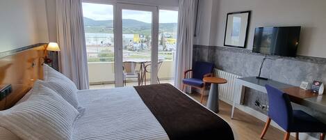 Habitación de hotel con cama, escritorio, silla, televisor y vistas al exterior.