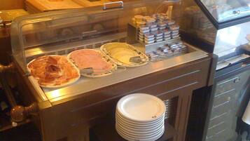 A buffet area with various food items and a stack of white plates.
