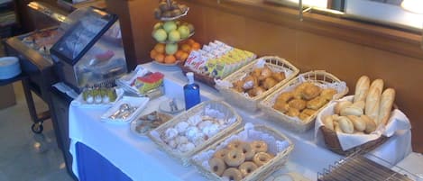 Una mesa de buffet con diversos alimentos, incluyendo frutas, pasteles y pan.