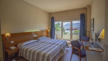 Ett hotellrum med två sängar, ett skrivbord med en stol, en TV och en balkong med utsikt över staden och bergen.