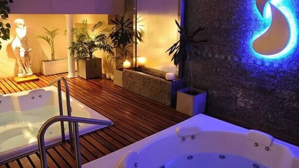 A spa area with two hot tubs, wooden flooring, and a wall with a large illuminated 'B' sign. - Ñikén Hotel & Spa (Necochea)
