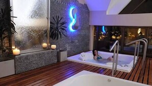 A spa area with a large bathtub, a smaller sitting tub, and a wall-mounted light fixture. - Ñikén Hotel & Spa (Necochea)