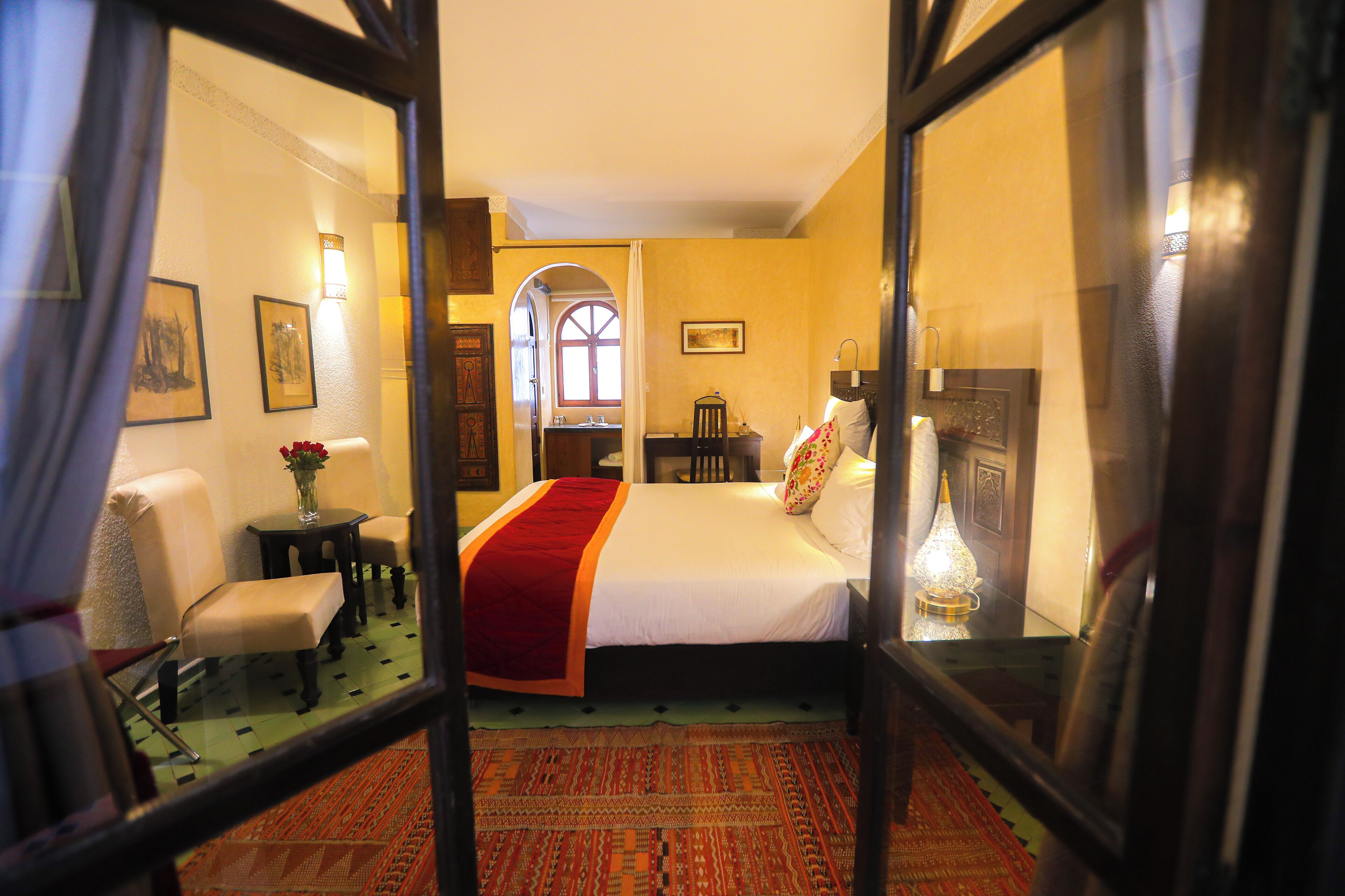 A hotel room with a bed, a chair, a small table, and a lamp.