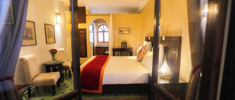 A hotel room with a bed, a chair, a small table, and a lamp.