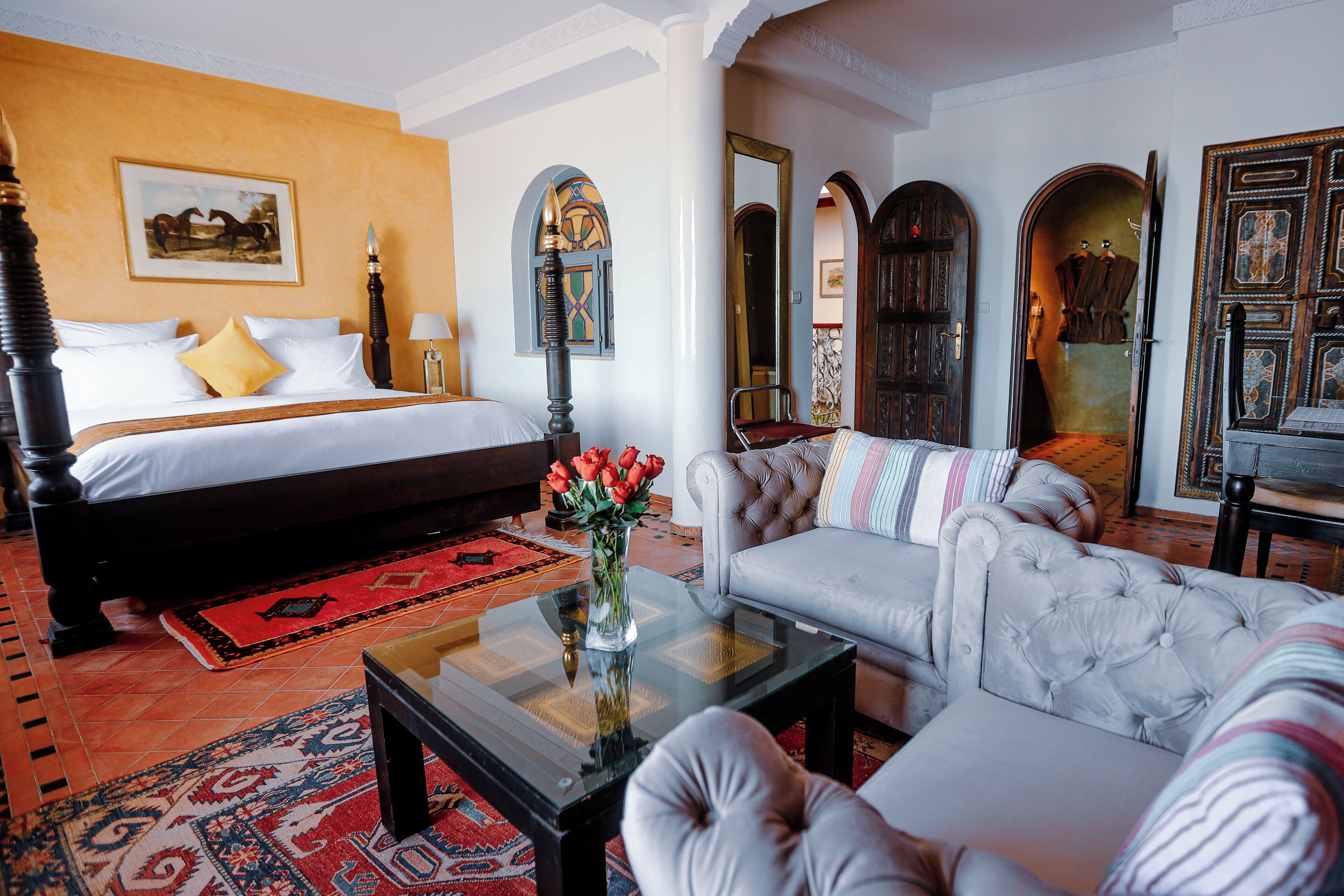 Habitación de hotel con cama, sofá, mesa de centro y un espejo decorativo.