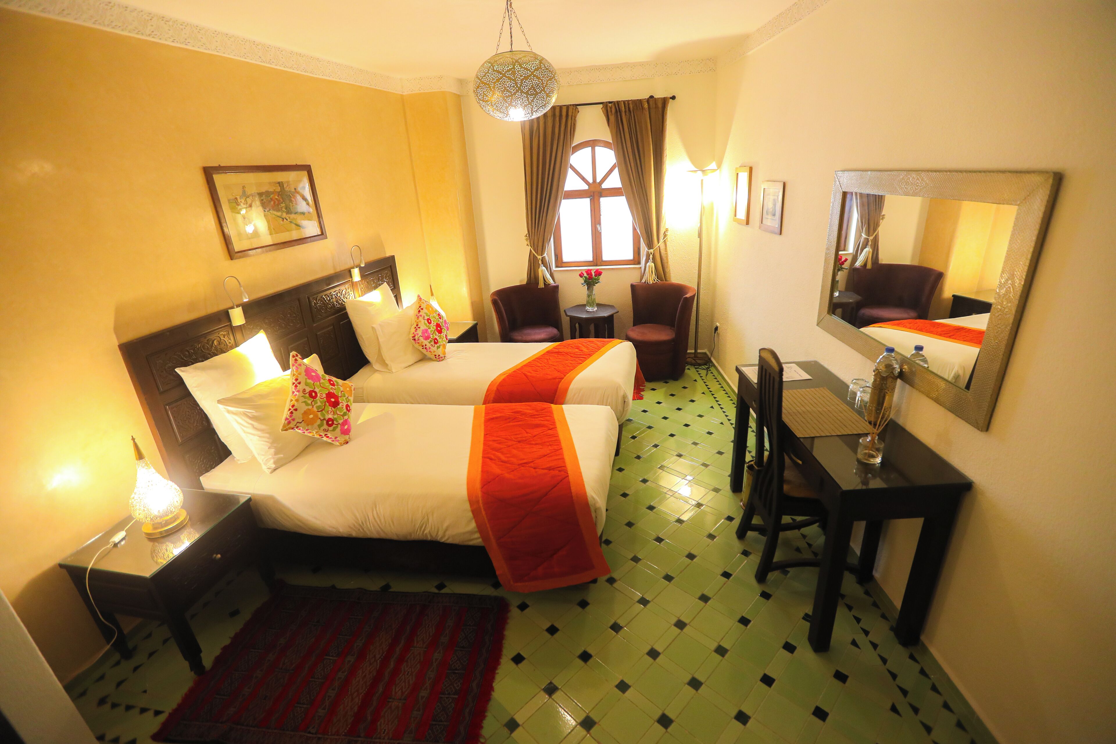 Habitación de hotel con una cama grande, dos sillas, una mesita, un espejo y una ventana con cortinas.