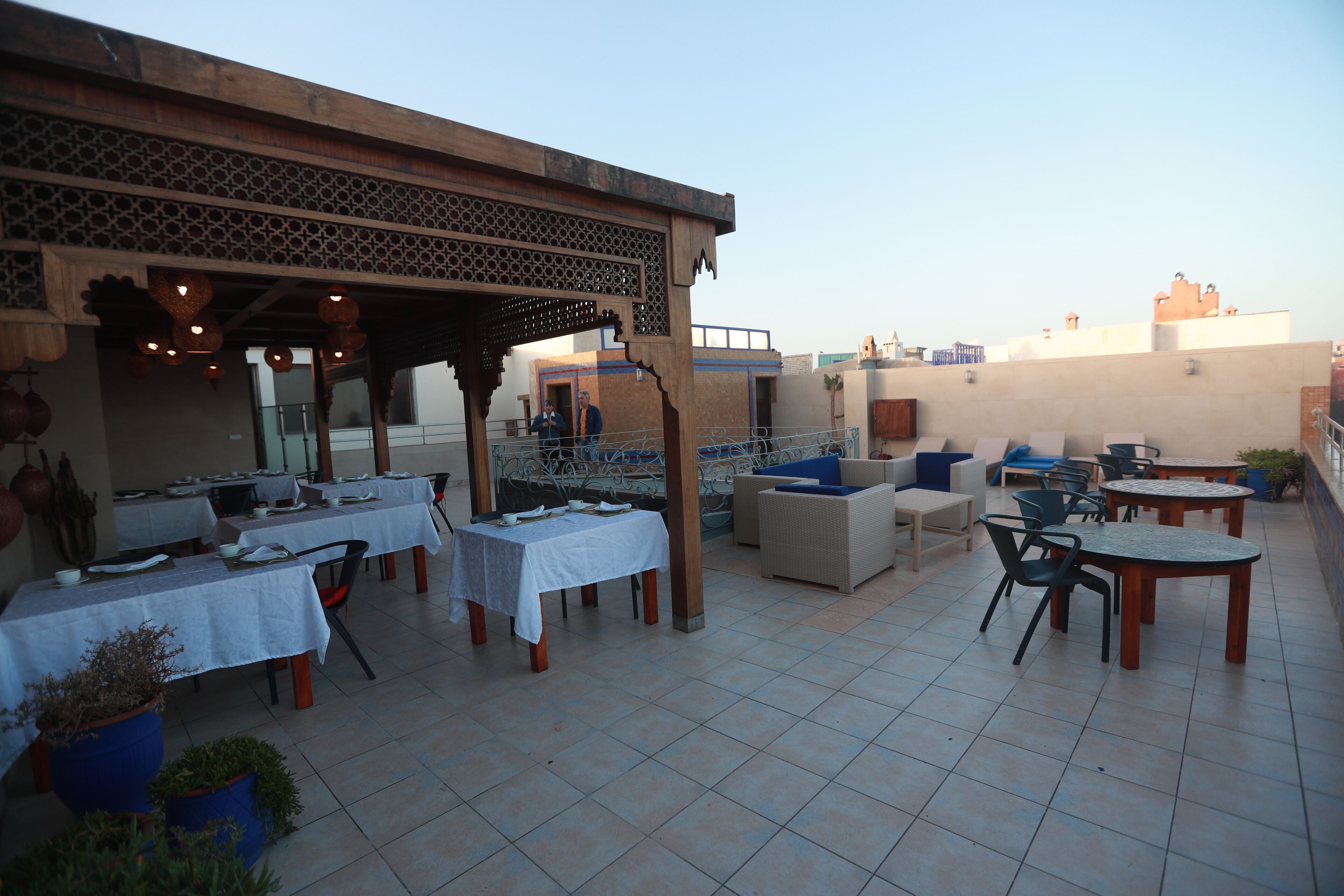 An outdoor dining area with tables and chairs, a covered seating area, and a view of the cityscape.