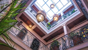Vista interior de un edificio con barandillas de hierro ornamentadas, tragaluces y lámparas colgantes.