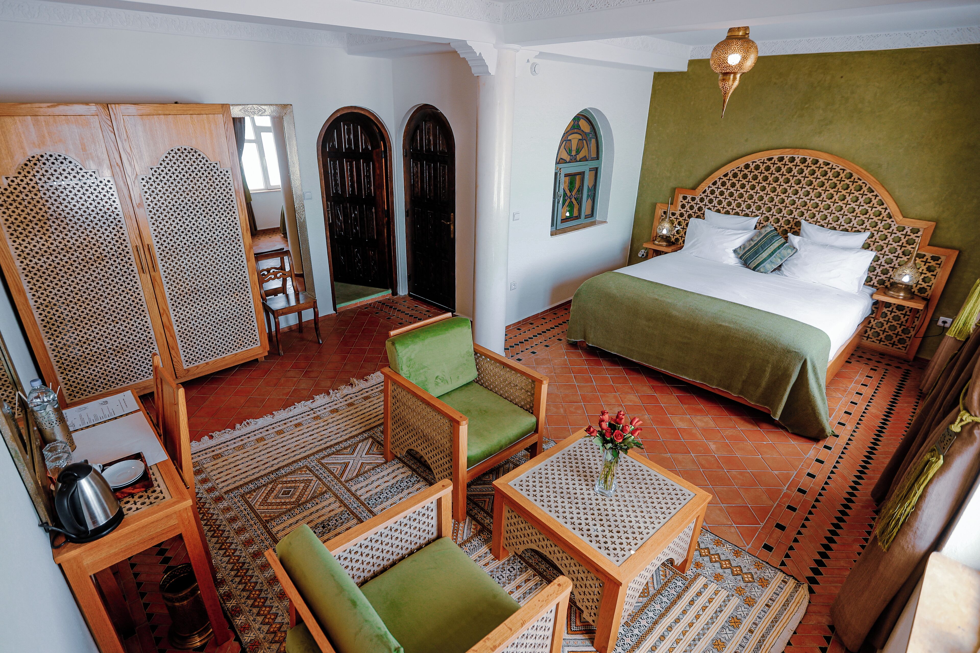 A room with a bed, green chairs, a small table, and a decorative wall.
