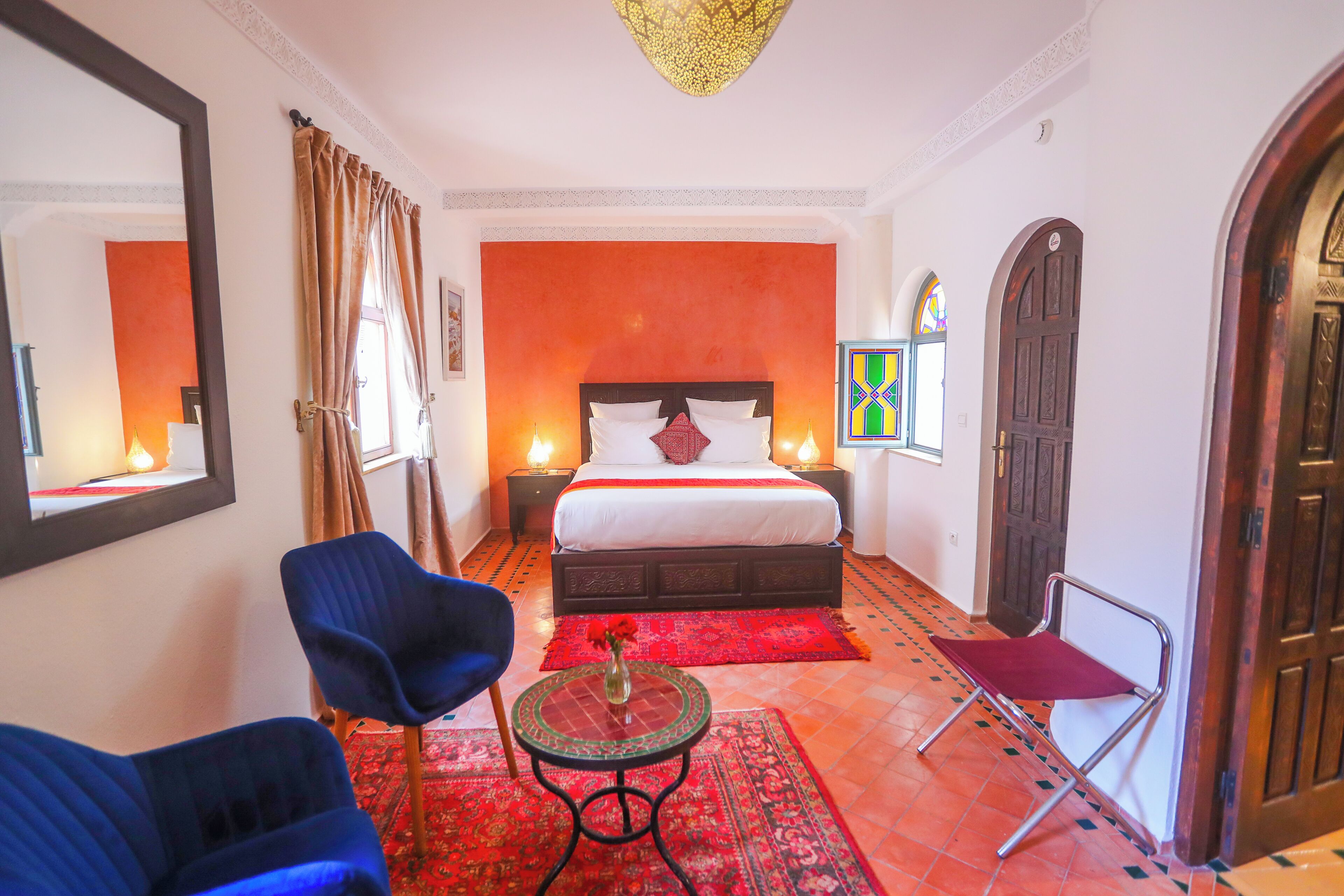 A hotel room with a large bed, two chairs, a small table with a vase, and a red rug.