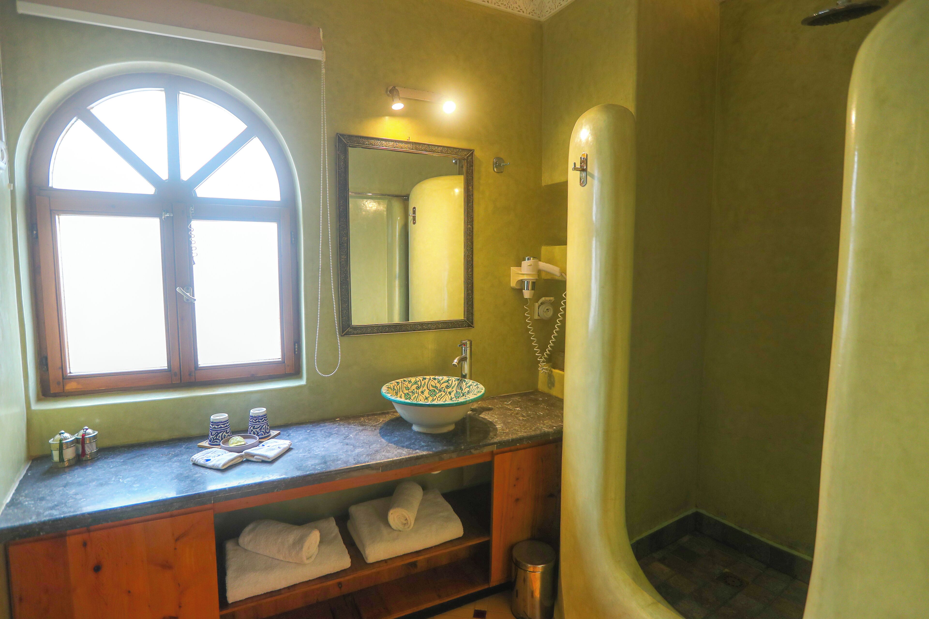 Un baño con un amplio ventanal de arco, un lavabo con un cuenco decorativo, un espejo y una zona de ducha.