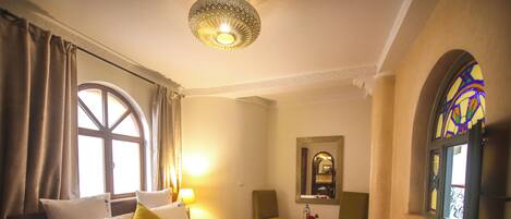 Une chambre d’hôtel avec un grand lit, une chaise, une petite table et une fenêtre ornée de vitraux.