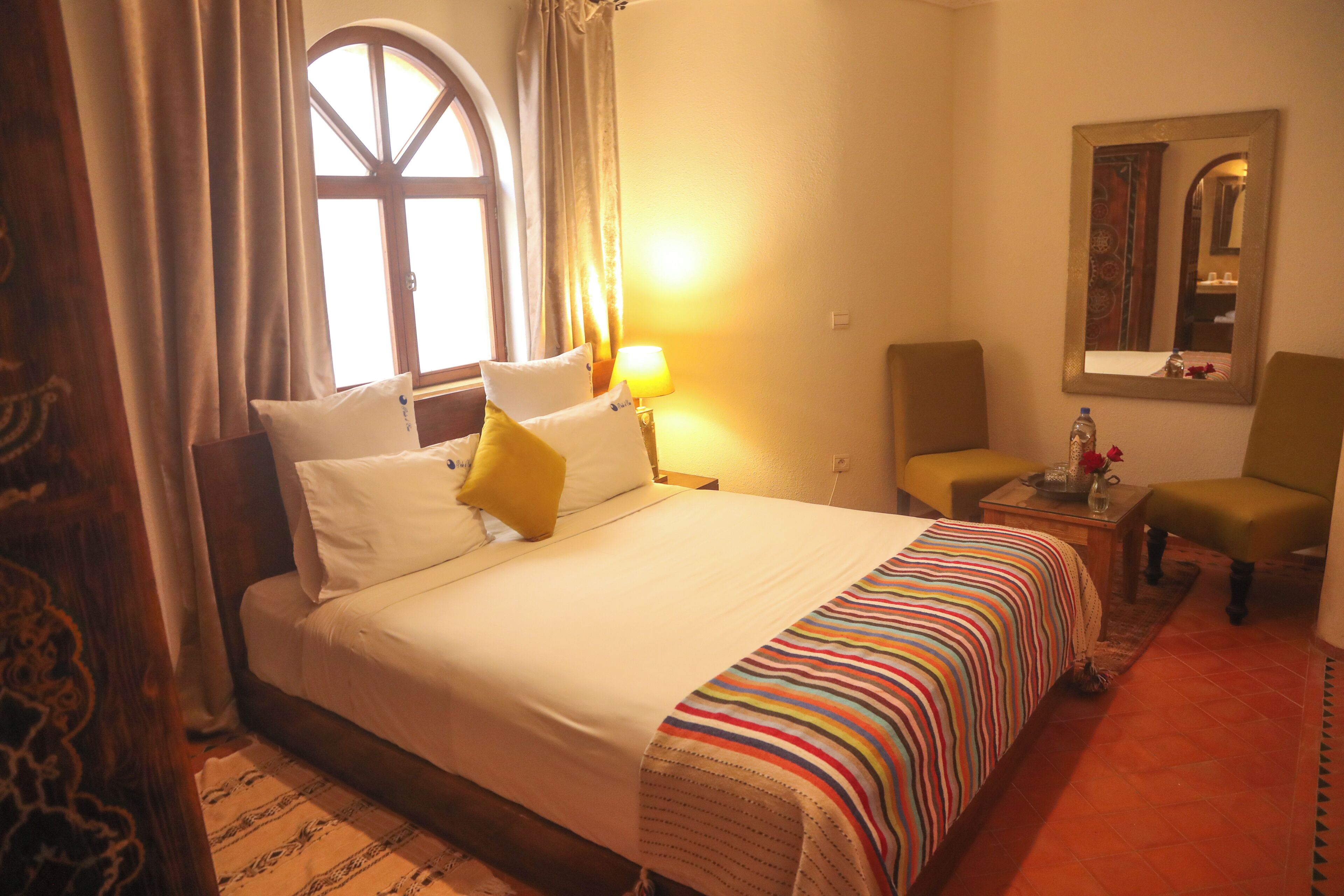 A hotel room with a large bed, a chair, a table, and a mirror.