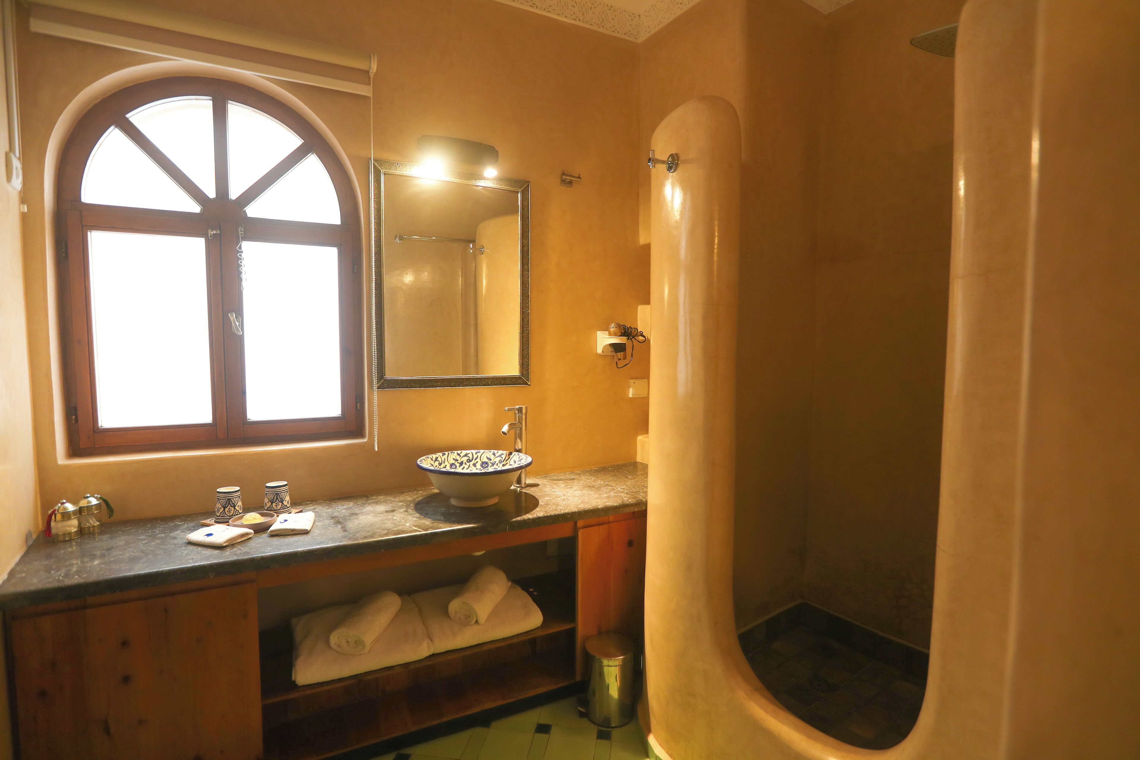 A bathroom with a large arched window, a sink with a bowl, a mirror, and a shower area.