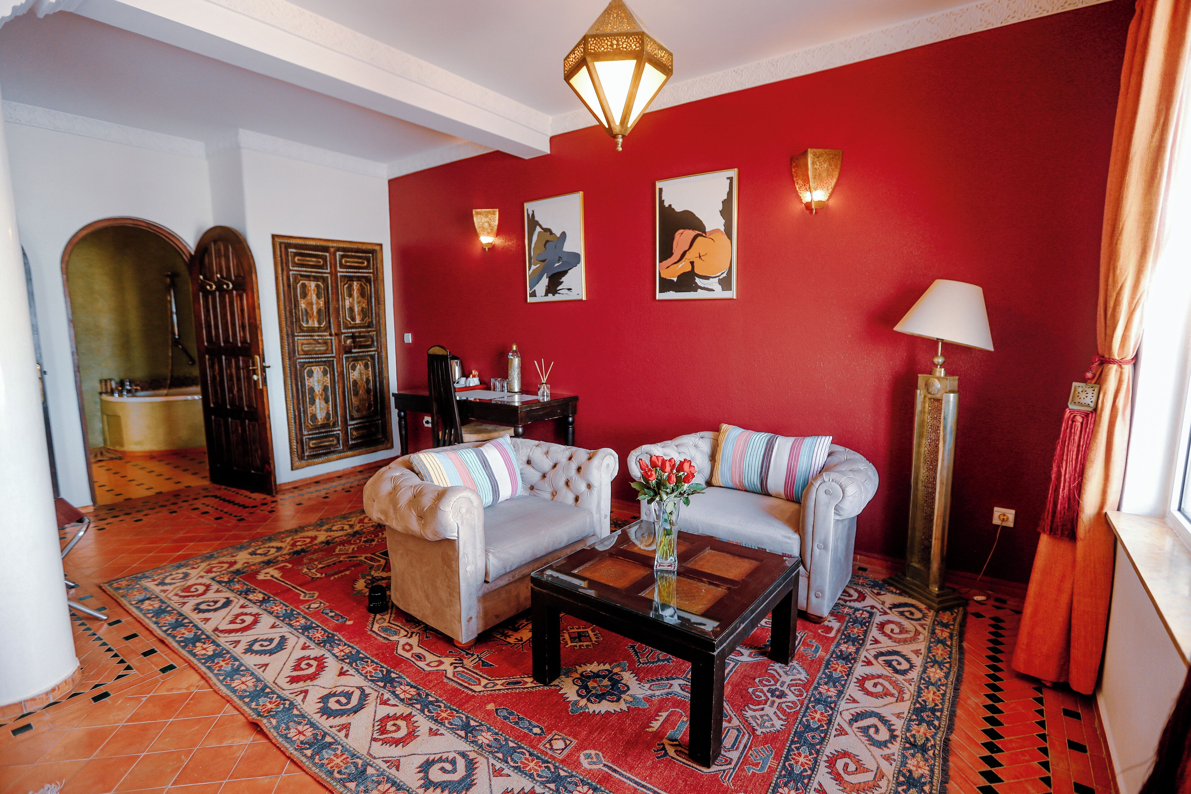 Una sala de estar con dos sofás, una mesita de centro, un tapete y una pared roja decorada con obras de arte.