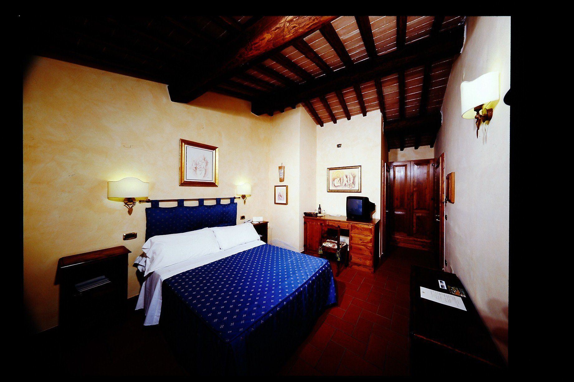 Une chambre d’hôtel comprenant un lit, des lampes de chevet, un bureau avec une télévision et une porte donnant sur une autre pièce.
