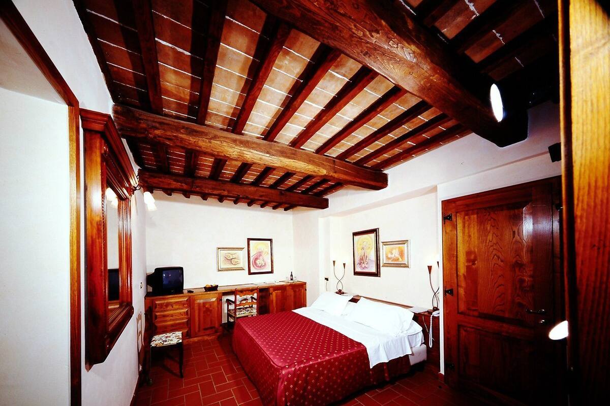 Una habitación con techo de madera, una cama con colcha roja, un escritorio con silla y una puerta de madera.